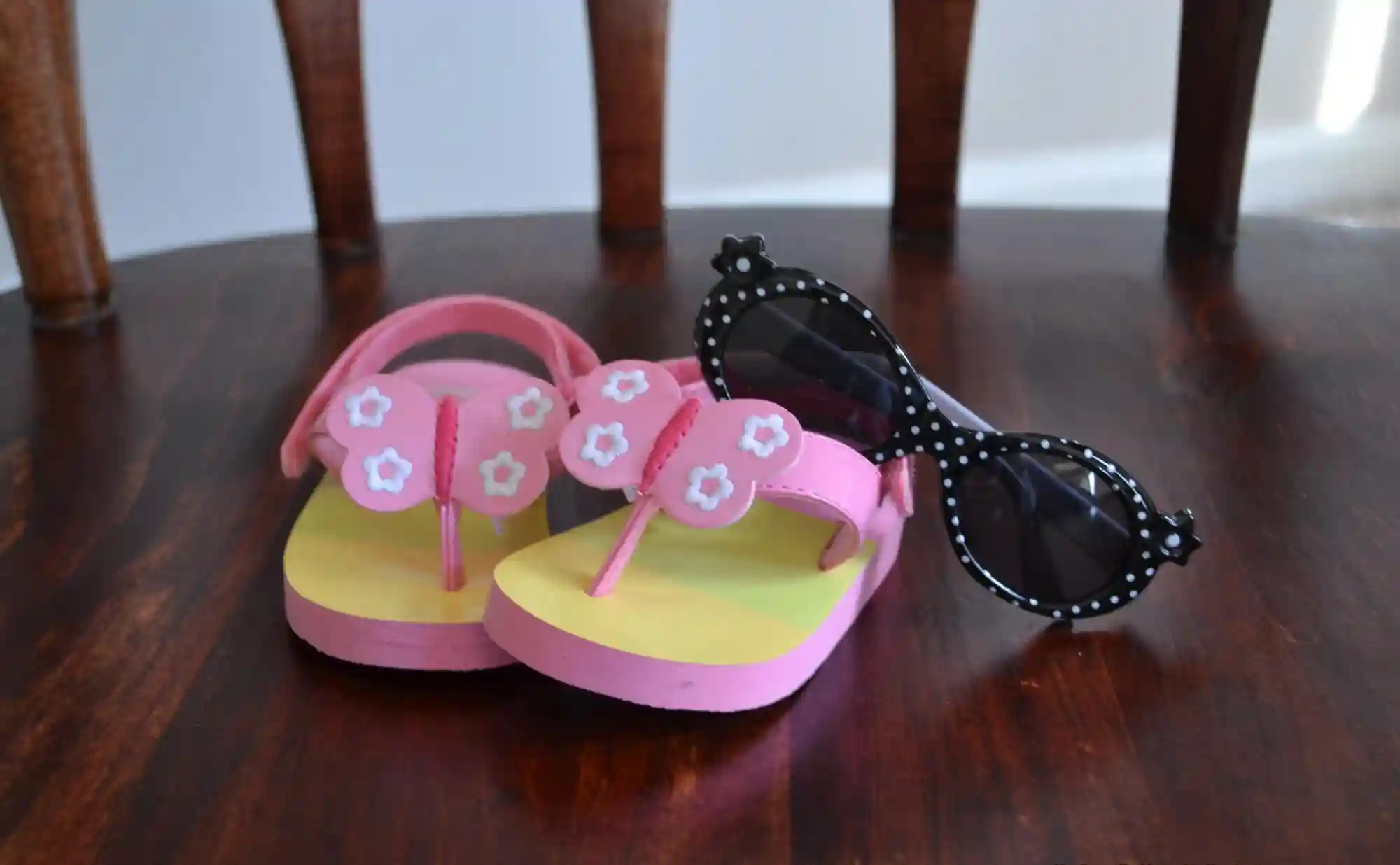 Chanclas rosas con mariposas y gafas de sol sobre una silla